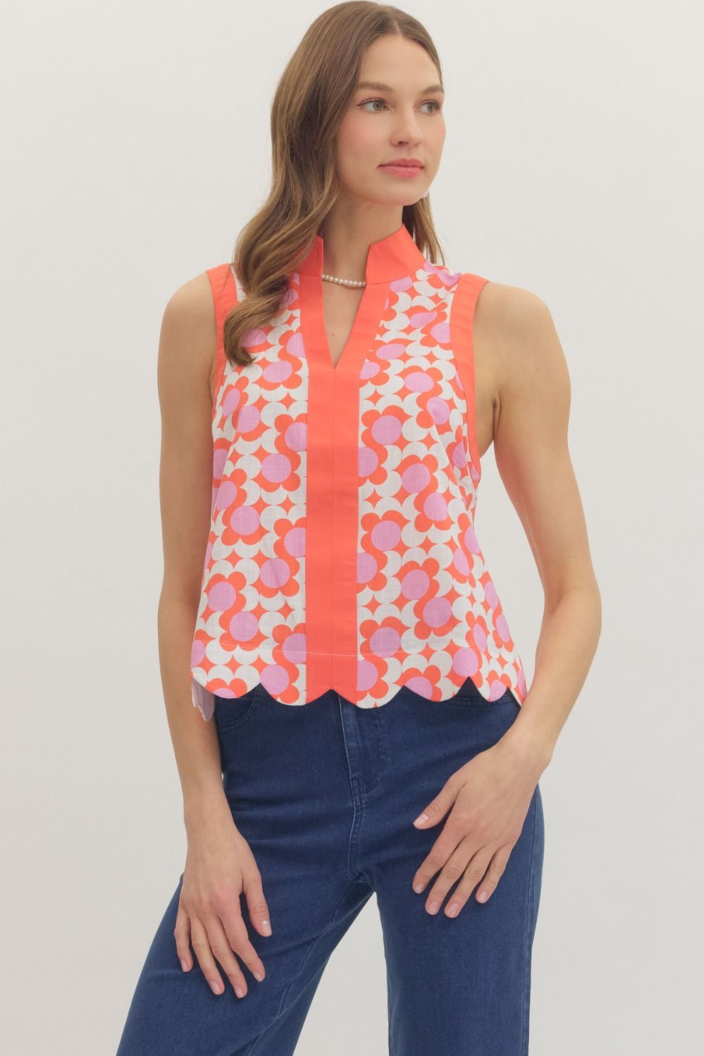 Woman wearing a sleeveless top with a colorful pattern and blue pants on a plain background