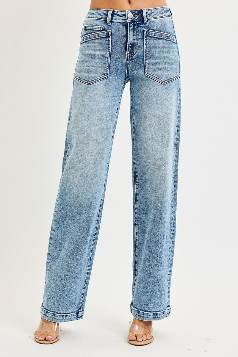 A model is wearing a pair of high-waisted, wide-leg light blue denim jeans with a faded wash and classic five-pocket styling, paired with clear high-heeled sandals against a plain white studio background.