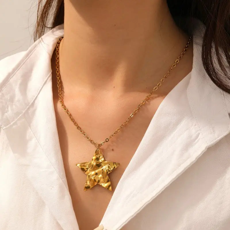 Gold star necklace worn by a person with a white shirt