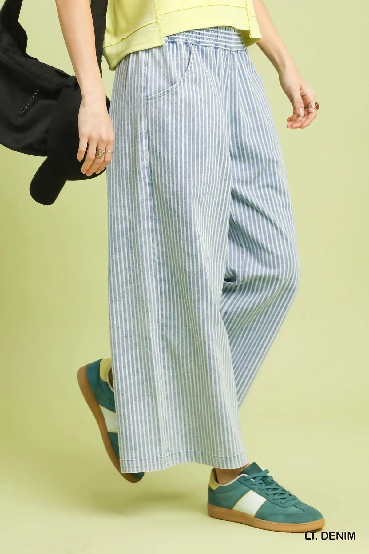Person wearing blue and white striped wide-leg pants with green sneakers on a light yellow background
