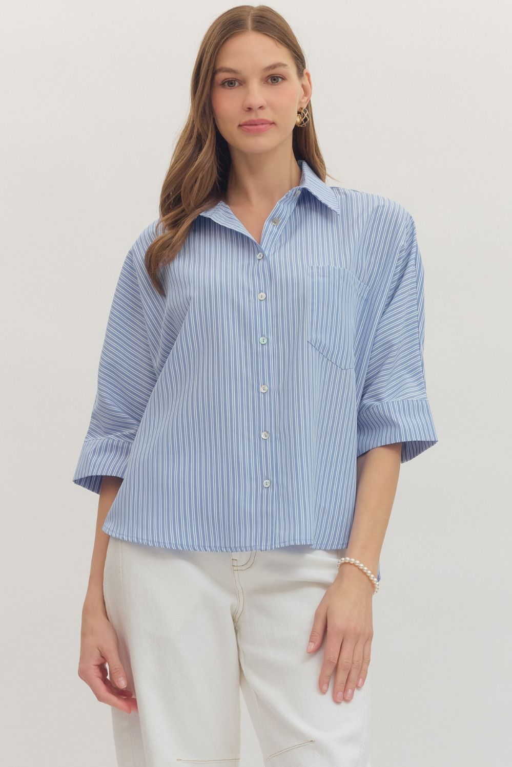 Woman wearing a blue striped shirt and white pants on a plain background