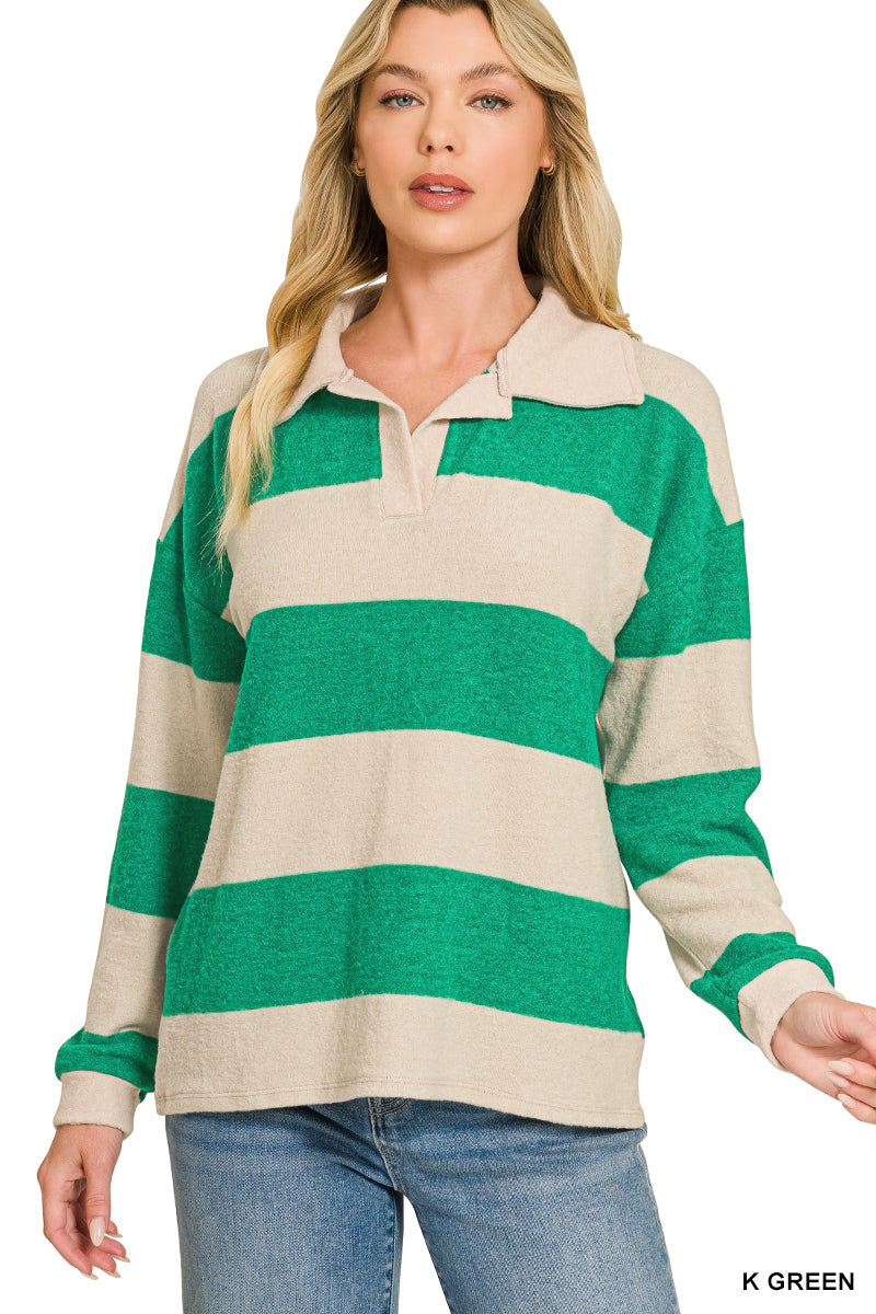 A woman modeling a long-sleeve rugby-style top with wide horizontal stripes in green and cream, paired with blue jeans against a plain white background.