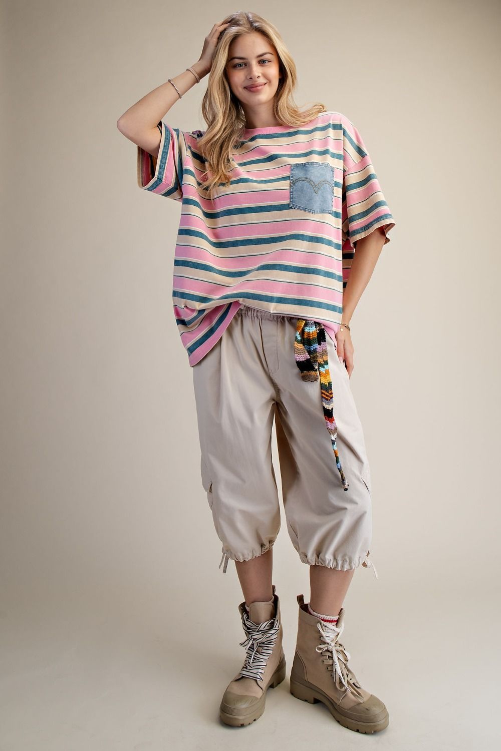 Woman wearing a colorful striped sweater and beige pants against a plain background