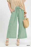 Person wearing green checkered pants with a beige top and holding a woven bag on a white background.