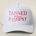 Light blue cap with pink 'Tanned & Tipsy' text on a beige background
