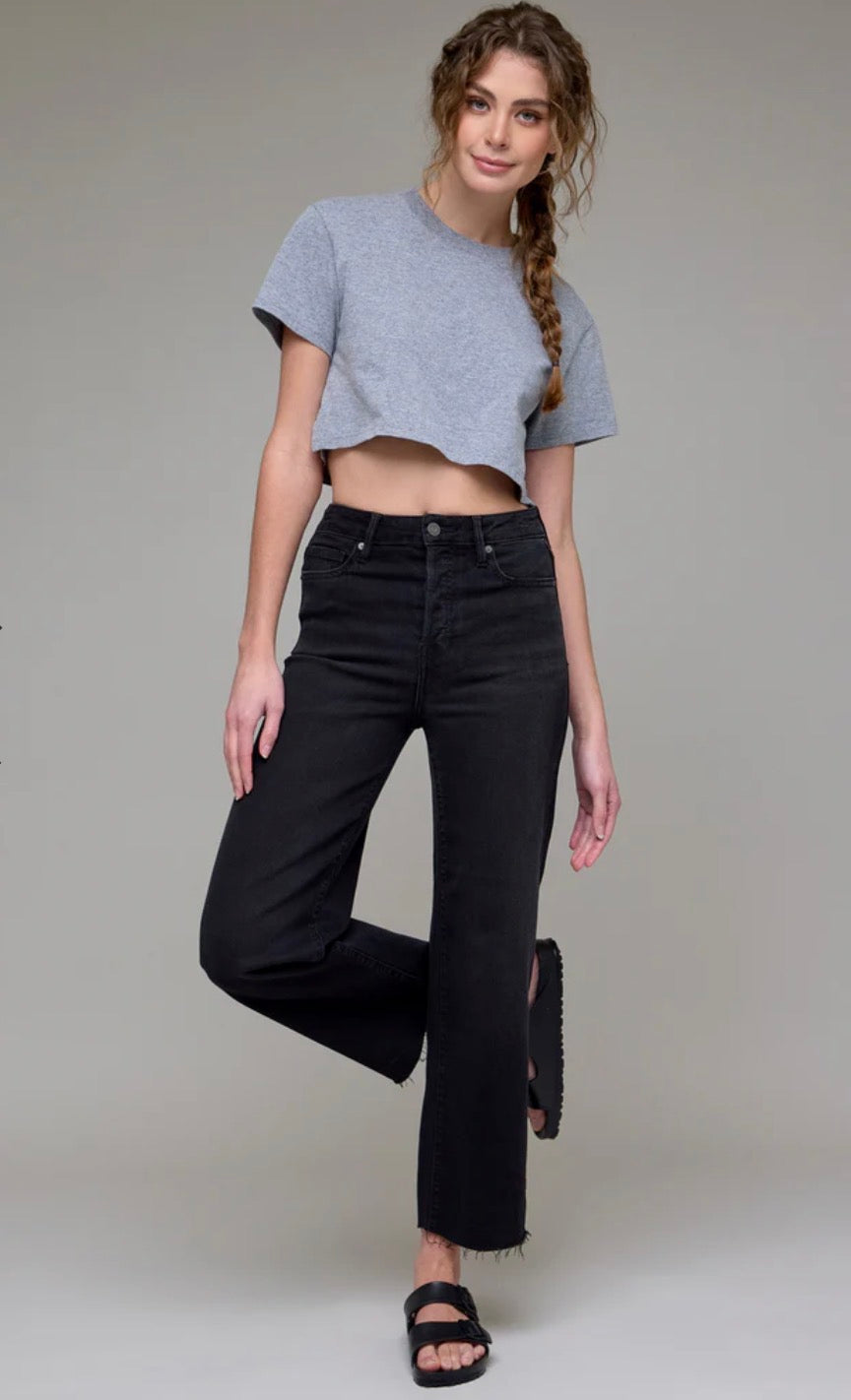 A woman modeling a light gray short-sleeve crop top and black wide-leg jeans against a plain light gray studio background.
