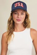 Woman wearing a navy cap with 'USA' in red on a plain background