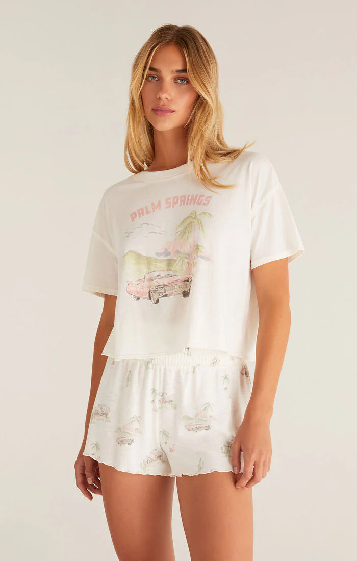 Woman wearing a white graphic t-shirt and shorts set with 'Palm Springs' text on a plain background