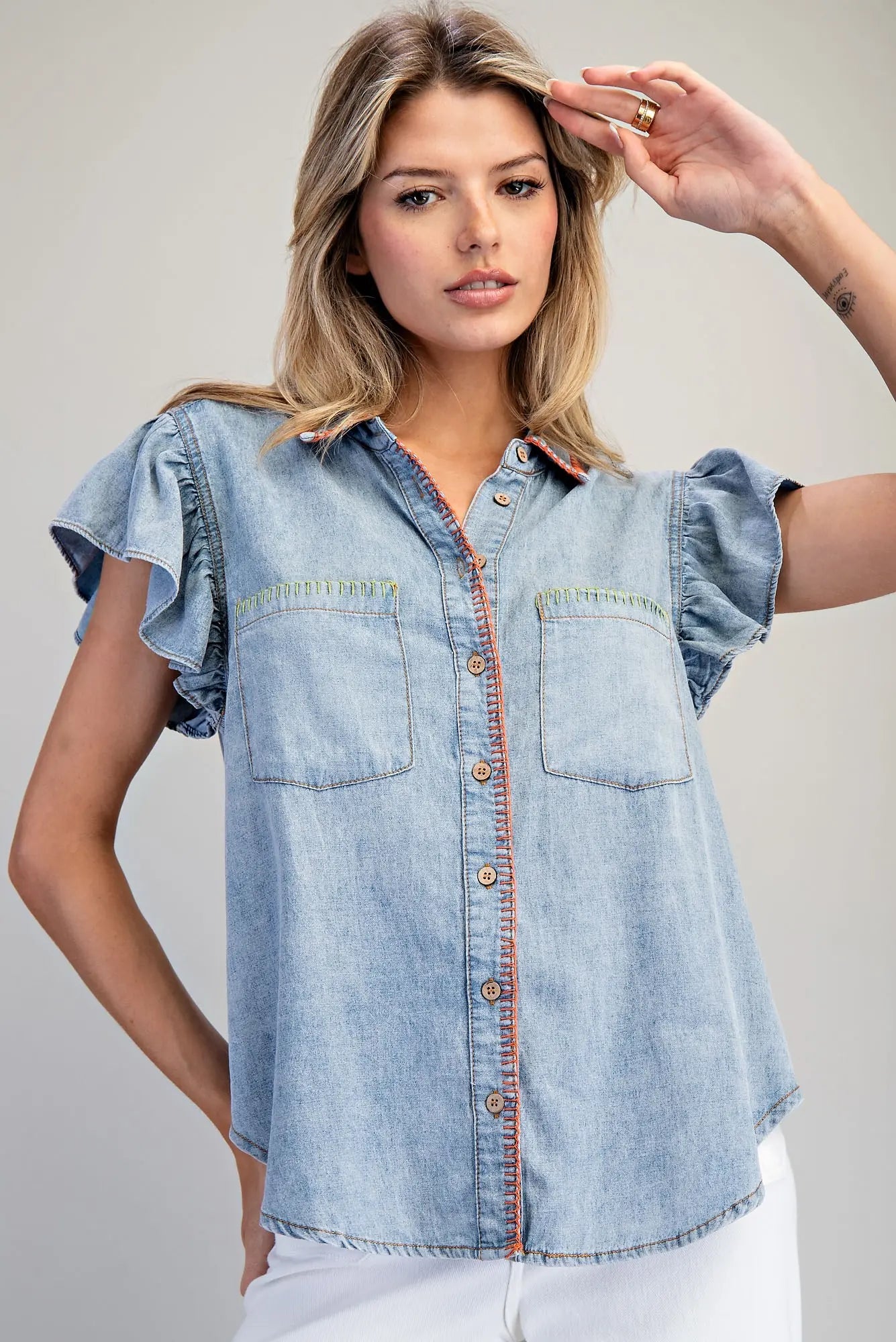 Woman wearing a denim shirt with ruffled sleeves against a plain background