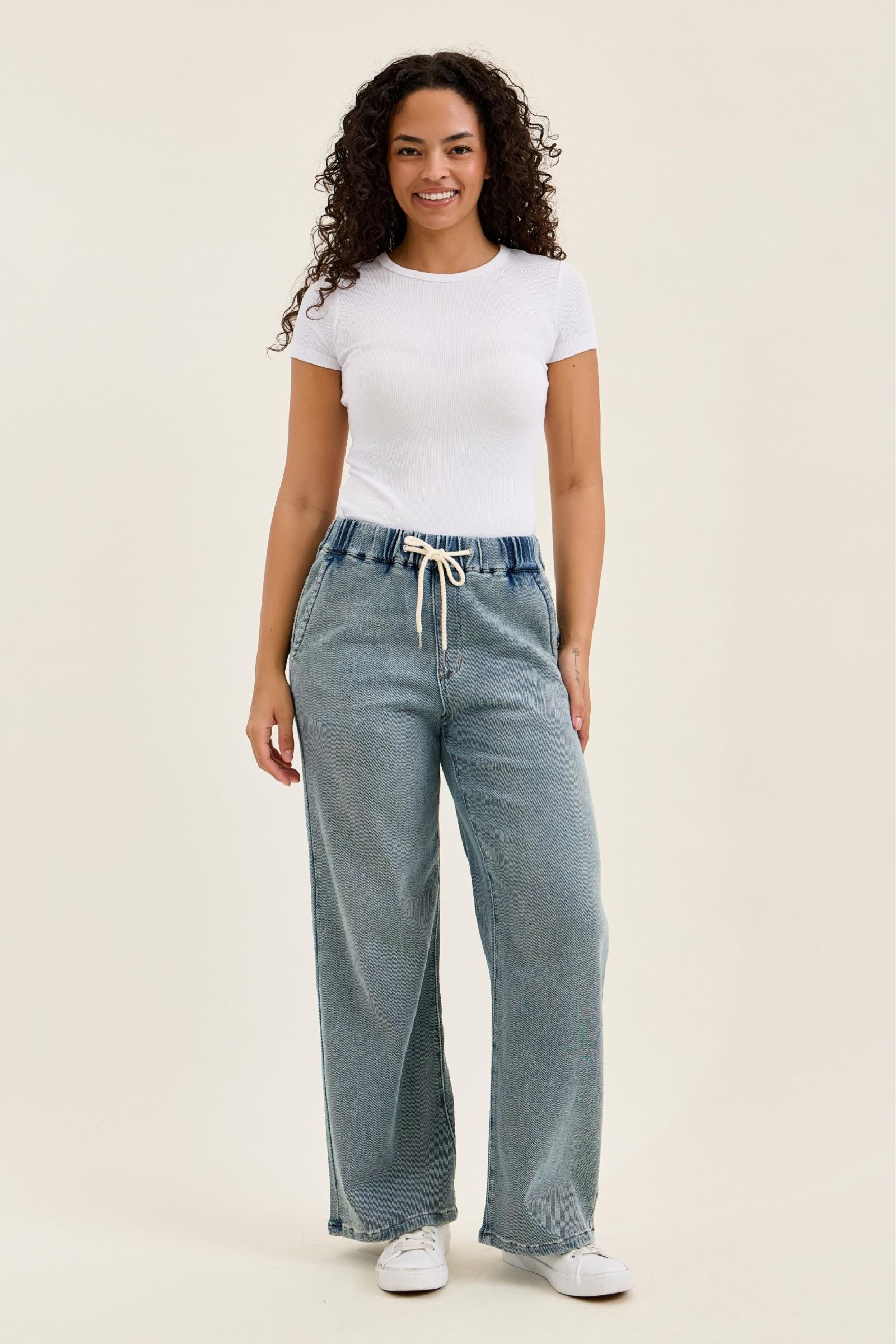 Woman wearing a white t-shirt and light blue jeans on a beige background