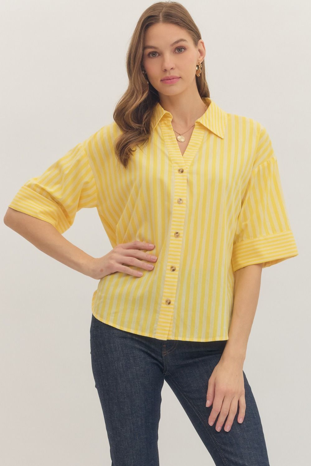 Woman wearing a yellow striped shirt and blue jeans on a plain background