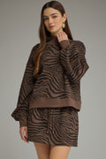 A woman modeling a brown and black zebra-print sweatshirt and matching mini skirt set against a solid gray studio background.