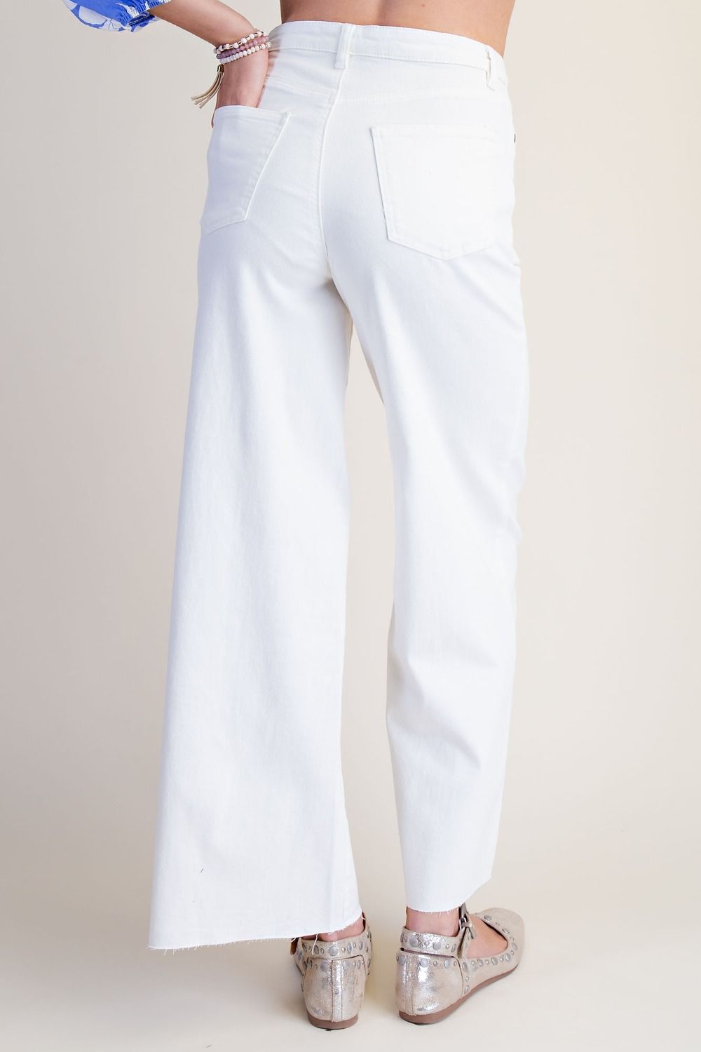 White wide-leg cropped pants shown from the back on a model, paired with metallic silver flat shoes against a light beige background.