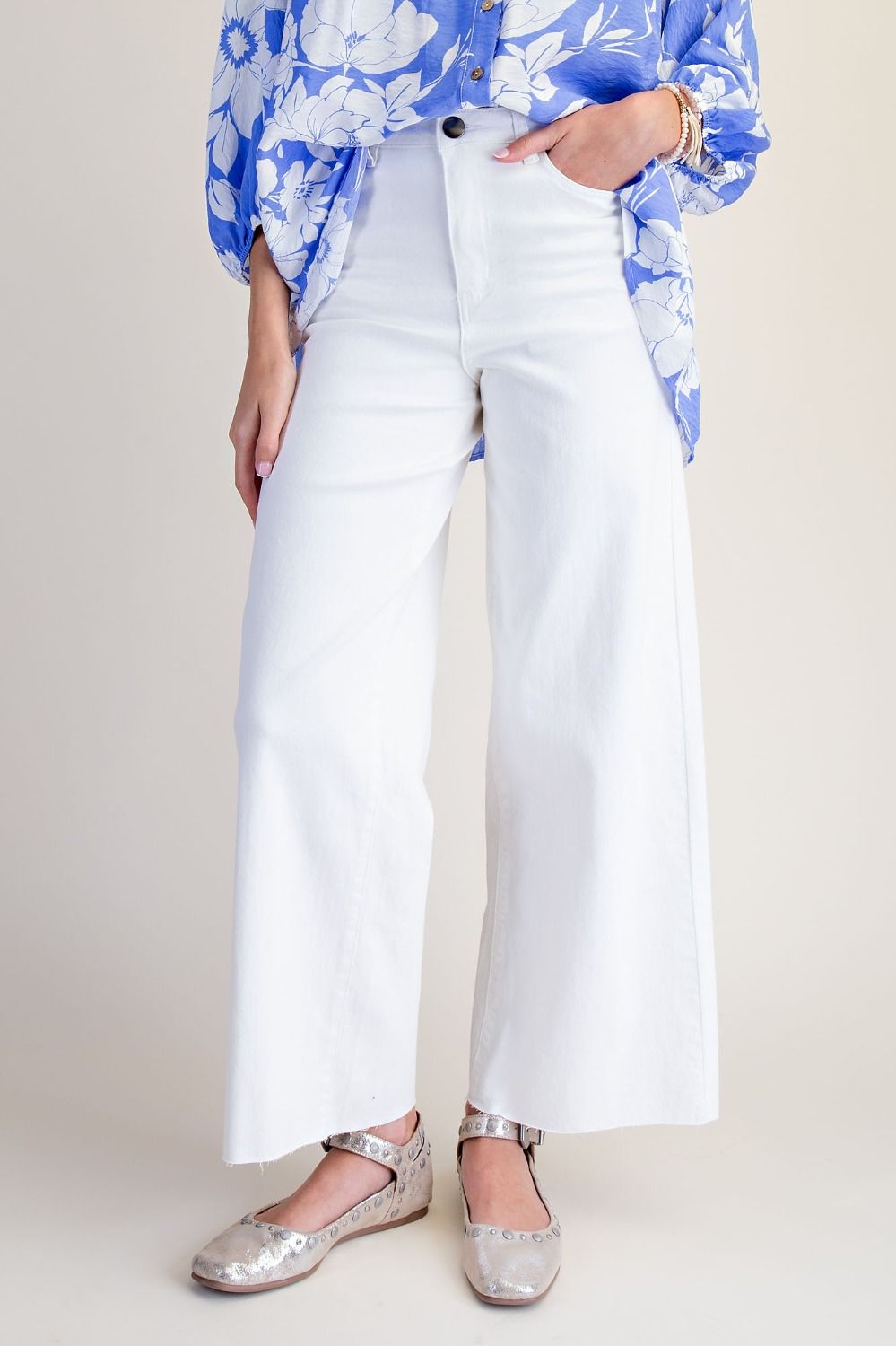 White wide-leg cropped pants worn with a blue floral blouse and metallic flats, shown on a model against a light beige studio background.