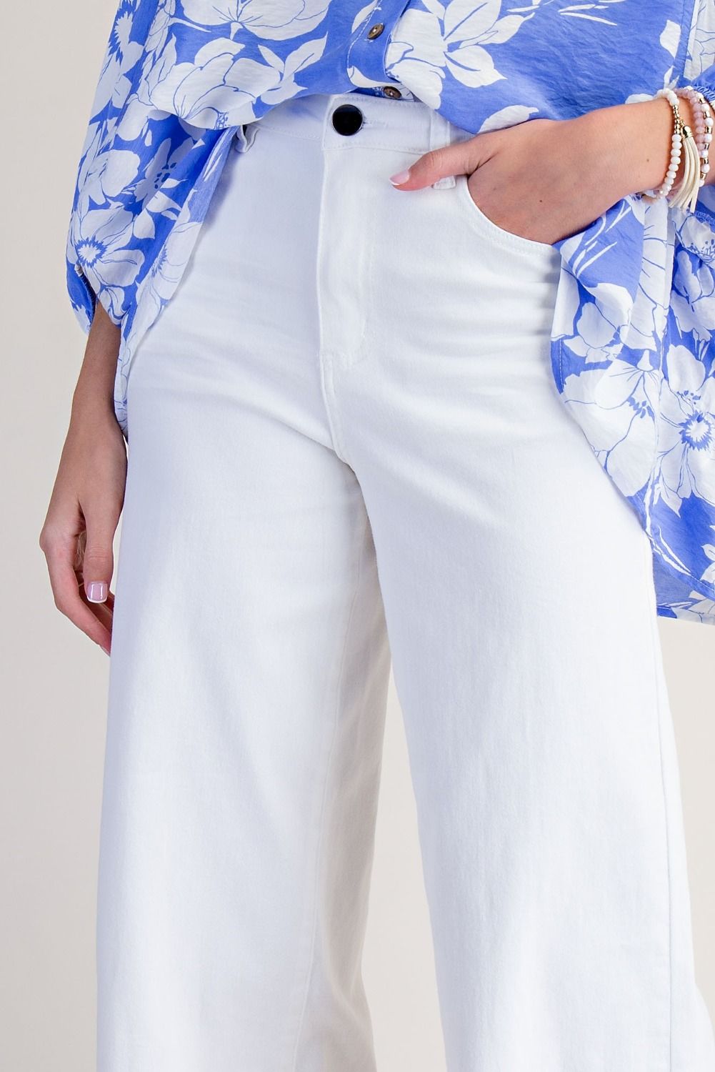 White wide-leg jeans worn by a model, paired with a blue and white floral shirt, shown from the waist down against a light beige background.