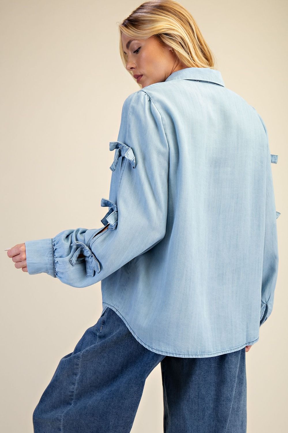 Woman wearing a light blue denim shirt with ruffled sleeves on a beige background