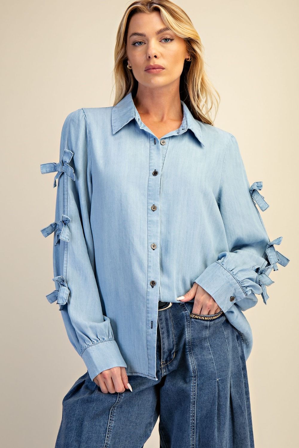 Woman wearing a light blue denim shirt with tassel details on a beige background