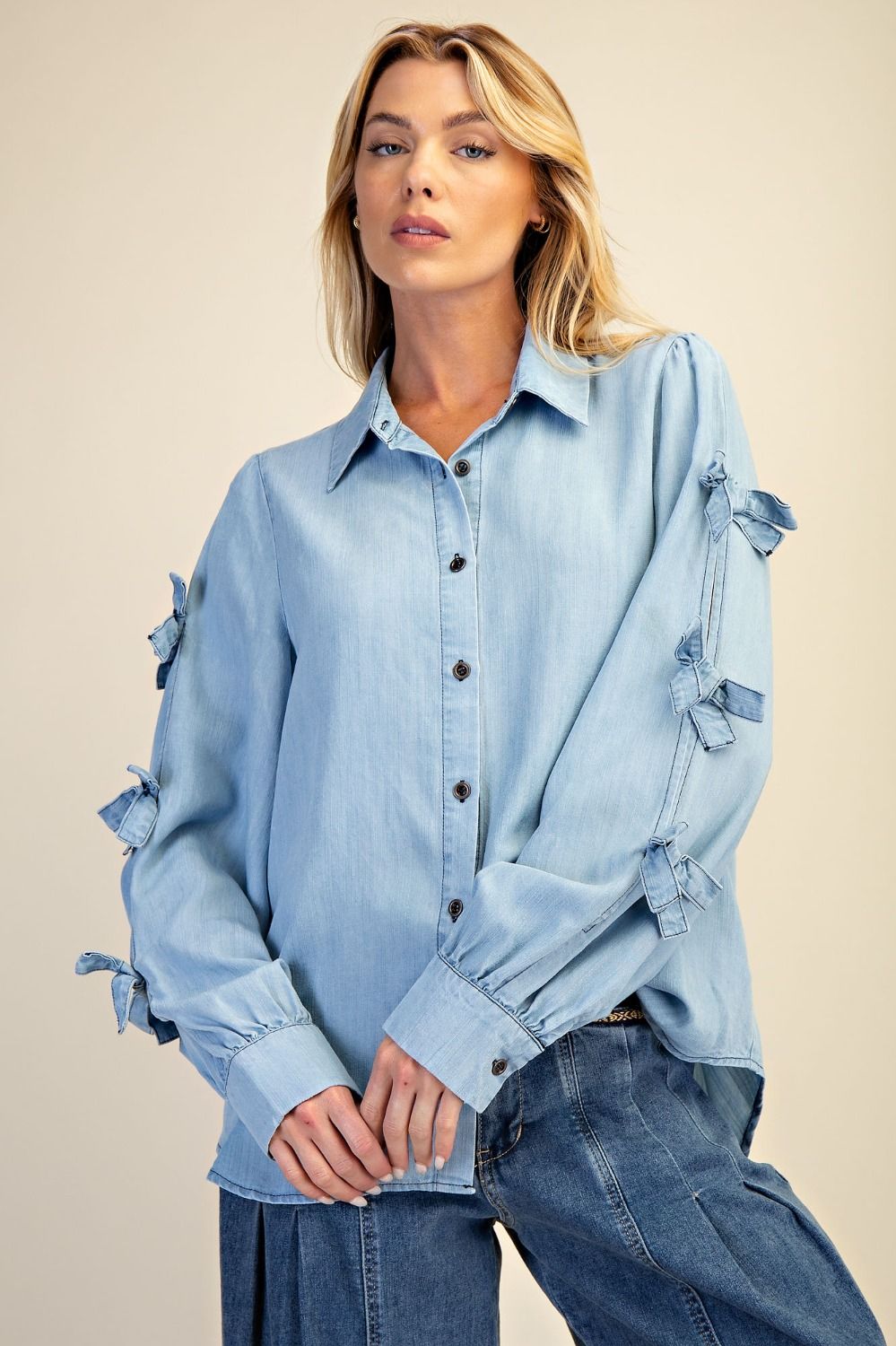 Woman wearing a light blue denim shirt with ruffled sleeves against a beige background