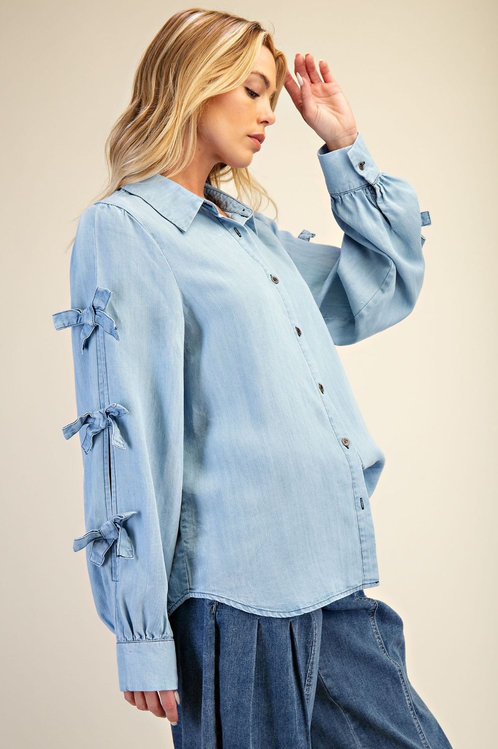 Woman wearing a light blue denim shirt with tie sleeves against a beige background