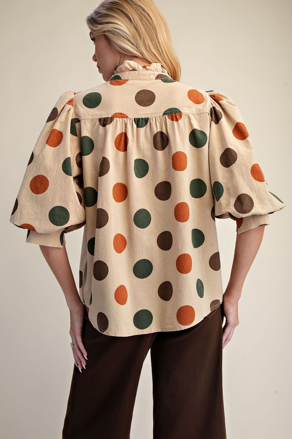 Woman wearing a polka dot blouse with puffed sleeves on a plain background