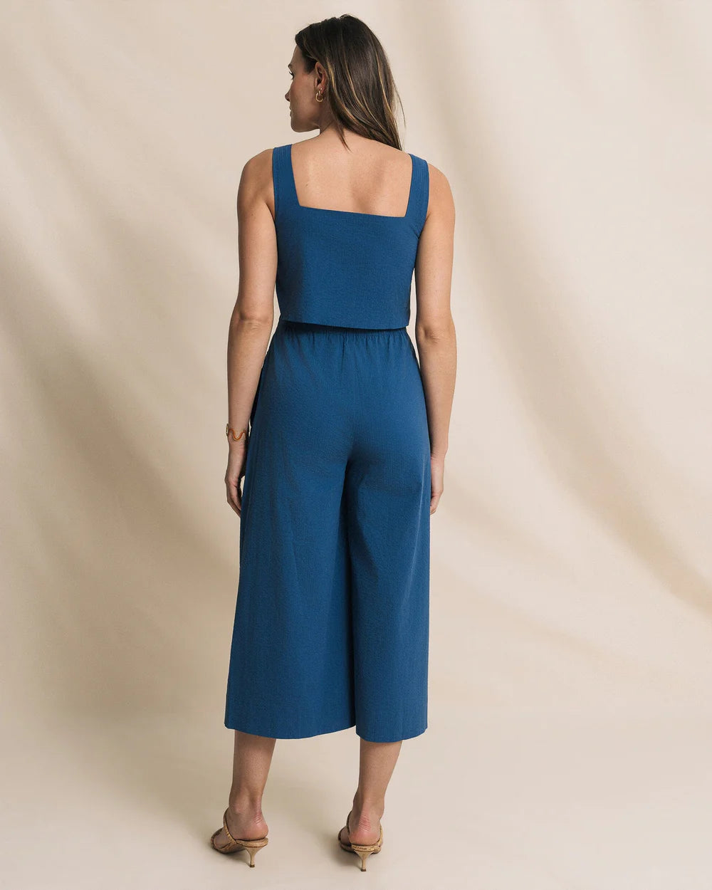 Woman wearing a blue jumpsuit against a beige background