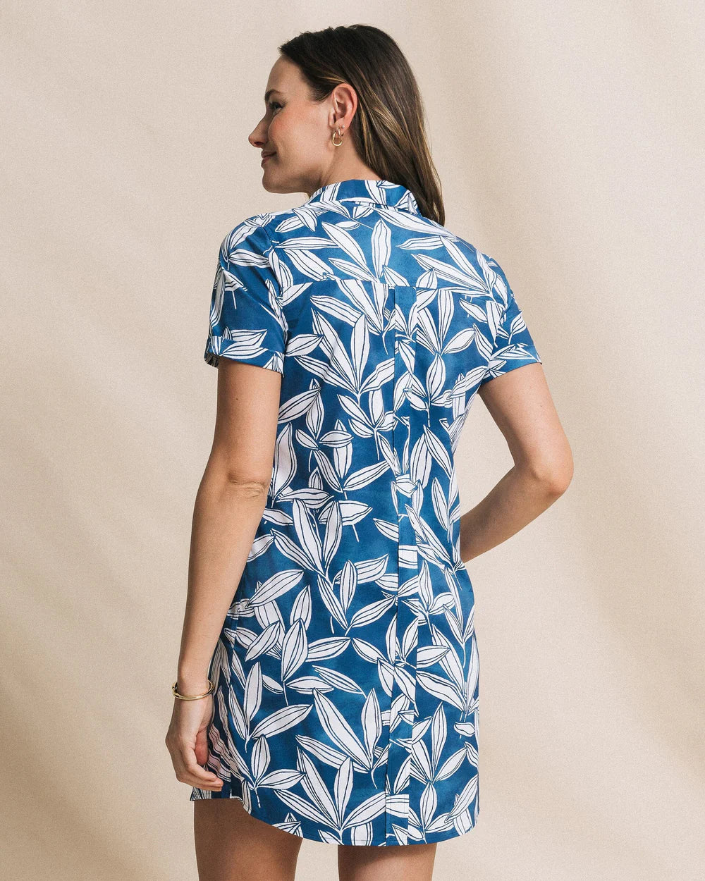 Woman wearing a blue and white leaf-patterned dress against a beige background