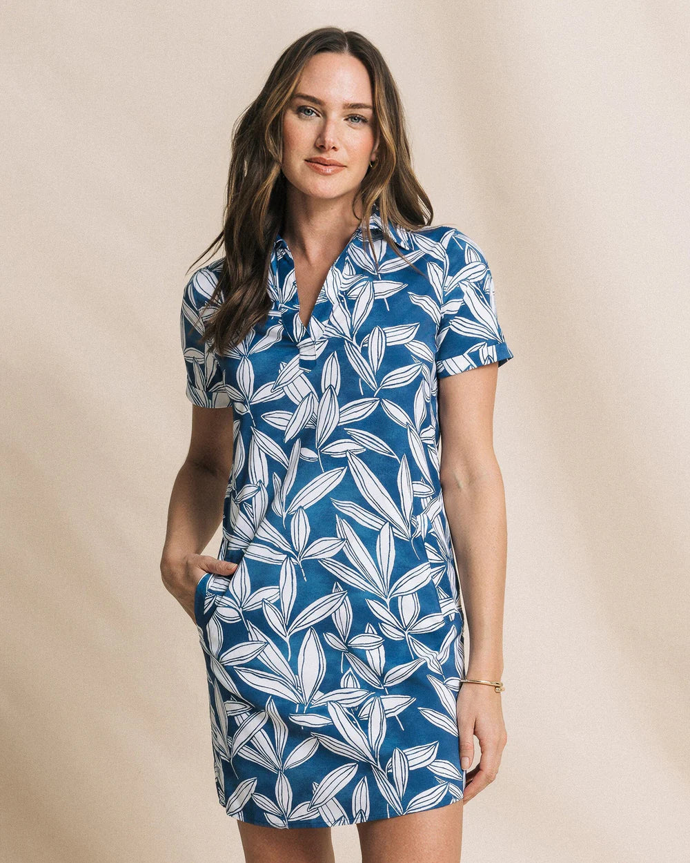 Woman wearing a blue and white leaf-patterned dress against a beige background