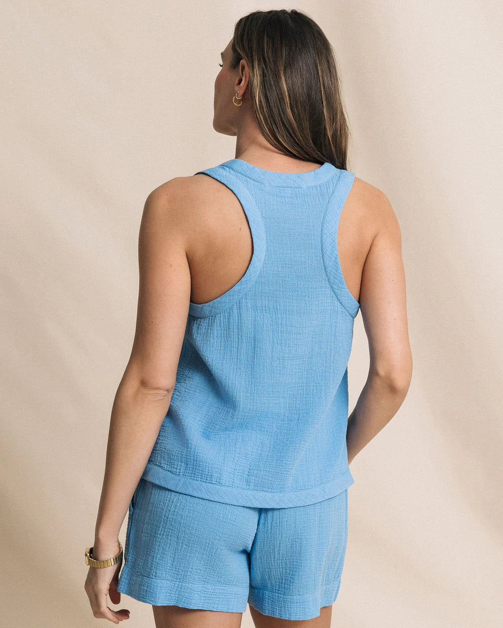 Woman wearing a blue sleeveless top and shorts set against a beige background