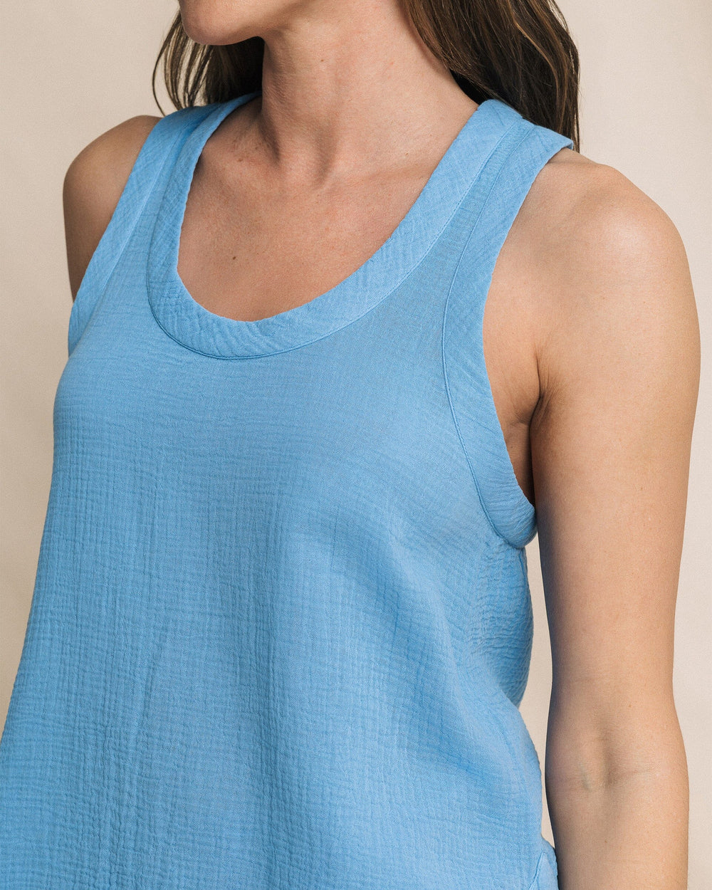 Close-up of a person wearing a blue tank top against a beige background