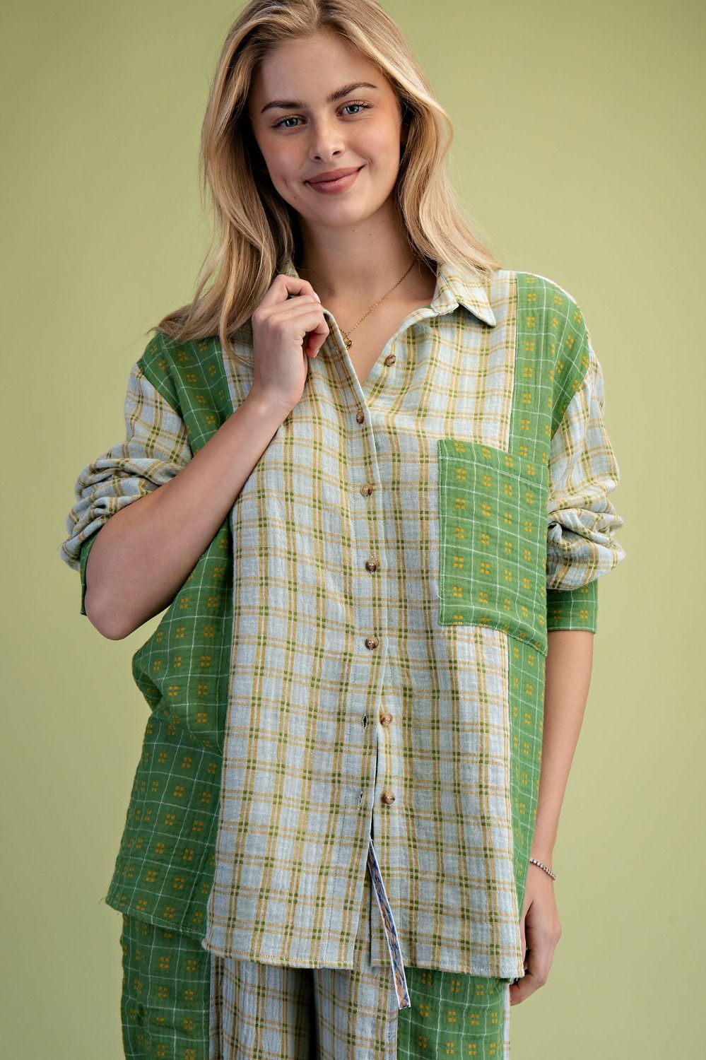 A woman modeling a green and yellow patchwork plaid button-up shirt and matching pants against a solid light green background.